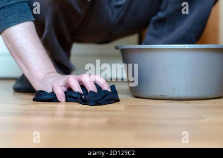 Le mani di un adulto stanno lavando il pavimento con un panno umido. Un uomo senza guanti sta pulendo la casa. Routine quotidiana a casa. Riprese a sinistra del pavimento Foto Stock