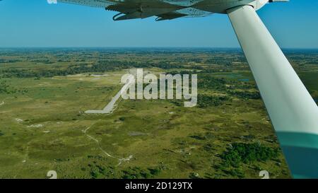 Vista aerea di un remoto campo d'aviazione circondato da macchia nel Delta di Okavango, Maun, Botswana dall'aereo. Foto Stock