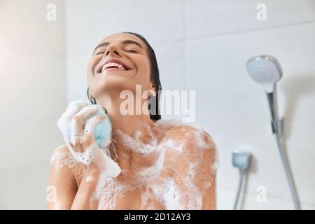 Gioiosa giovane donna che lava il suo corpo con la loofah da bagno Foto Stock