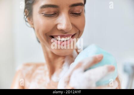 Giovane donna allegra che lava il corpo con la loofah da bagno Foto Stock
