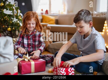 Bambina e ragazzo in pigiama all'interno a casa a Natale, regali di apertura. Foto Stock