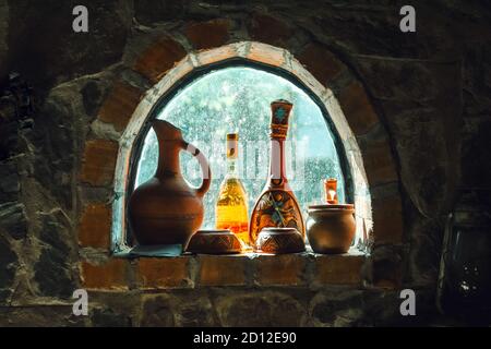 Vecchie bottiglie di vino rustiche, brocche su una piccola cantina finestra su un muro di pietra Foto Stock