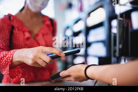 Donna con maschera viso a pagamento da smartphone all'interno del centro commerciale, concetto di coronavirus. Foto Stock