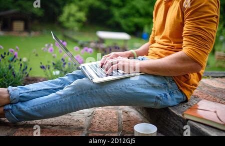 Uomo irriconoscibile con computer portatile che lavora all'aperto in giardino, concetto di home Office. Foto Stock