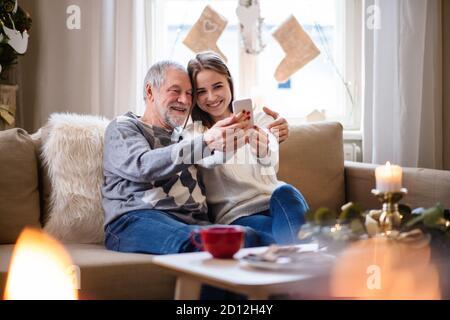 Giovane donna con nonno in casa a Natale, prendendo selfie. Foto Stock