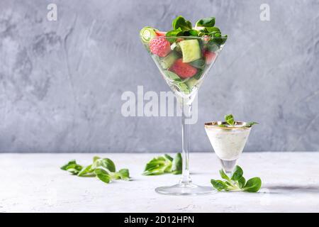 Primavera Estate la dieta con insalata di fragole, cetriolo, verde insalata di campo e yogurt salsa alla menta servito in bicchiere da cocktail su grigio Sfondo texture. C Foto Stock