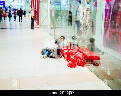 Sochi, Russia - 14 dicembre 2019. I bambini si siedono sul pavimento con gli acquisti vicino alla vetrina di un negozio in un centro commerciale Foto Stock