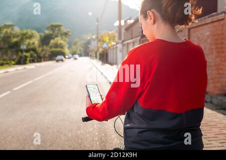 Una donna ha uno smartphone con un'app mappa online. Vista posteriore. Sullo sfondo c'è una strada cittadina. Il concetto di navigazione Internet e tecnologia moderna Foto Stock