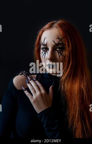 Halloween zenzero donna strega con lunghi chiodi spaventosi e moda Halloween compongono. Sfondo nero. Foto Stock