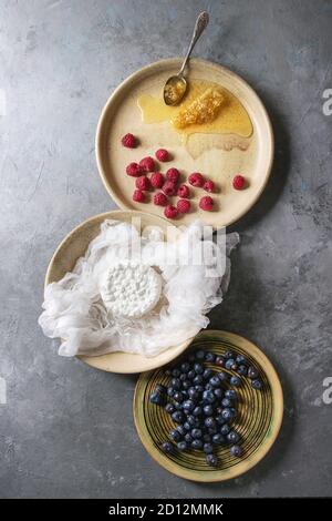 Freschi Fatti in casa cottage cheese nel buratto servito in tazza ceramica con mirtilli, lamponi e favi su grigio Sfondo texture. Top vie Foto Stock