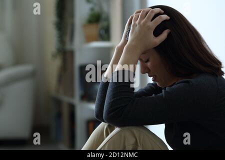 Ritratto di profilo di una donna disperata triste che si lamenta da sola il buio a casa di notte Foto Stock