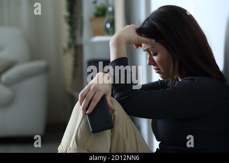 Donna triste che tiene lo smartphone lamentarsi da sola a casa la notte Foto Stock