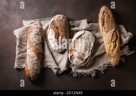 Varietà di polpettine sfornato fresco artigianale di segale e grano intero pane sulla tela di lino su marrone scuro dello sfondo texture. Vista superiore, copia dello spazio. Foto Stock