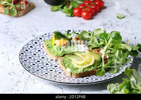 Sandwich vegetariano con avocado, ricotta, tuorlo d'uovo, spinaci, pomodori ciliegia sul grano intero pane tostato su piastra in ceramica con gli ingredienti sopra uovere Foto Stock