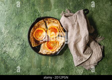 In casa Crepes Pancake servita in ghisa padella con sanguinose arance e sciroppo di rosmarino con fette di arance rosse di Sicilia su una texture verde sullo sfondo Foto Stock