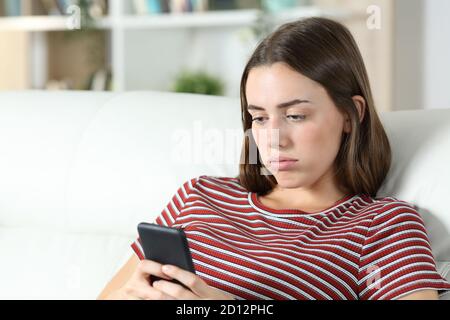 Annoiato teen che controlla il contenuto dello smartphone seduto su un divano a casa Foto Stock