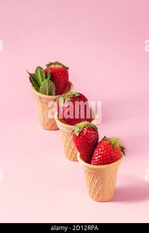 Fragole fresche in tazze waffle su rosa pastello pin-up dello sfondo. Copia dello spazio. Foto Stock