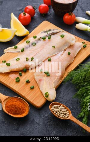 Filetto di eglefino fresco crudo su tagliere di legno con spezie ed erbe Foto Stock