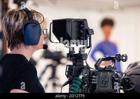 Un primo piano di una cameraman, indossando una cuffia che guarda attraverso il mirino della videocamera durante la ripresa di un programma televisivo. Foto Stock