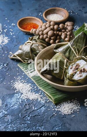 Riso asiatico piramidal gnocchi di patate al vapore dal riso farina di tapioca con ripieno di carne in foglie di banano servito in tazza di ceramica. Ingredienti e salse al di sopra Foto Stock