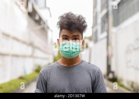 Giovane uomo asiatico con capelli ricci che indossa la maschera strade Foto Stock