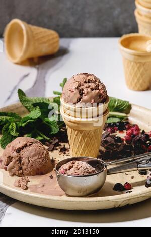 Cioccolato artigianale gelato al lampone in piccoli waffle cup servita con frutti di bosco surgelati, menta fresca, cioccolato fondente tritato e il cucchiaio di metallo in ceramica p Foto Stock