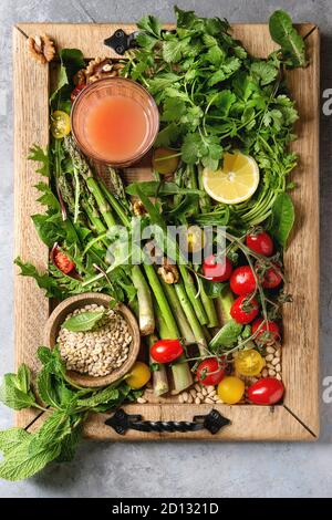 Varietà di piatti vegetariani mangiare sano ingredienti alimentari. Asparagi verdi, erbe aromatiche, pomodori, dadi, frumento calli, tarassaco foglie, bicchiere di succo di frutta su legno t Foto Stock