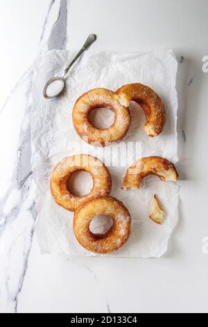 In casa della pasta sfoglia fritti ciambelle o cronuts con zucchero su carta sgualcita su marmo bianco sullo sfondo di texture. Appartamento laico, spazio. Foto Stock