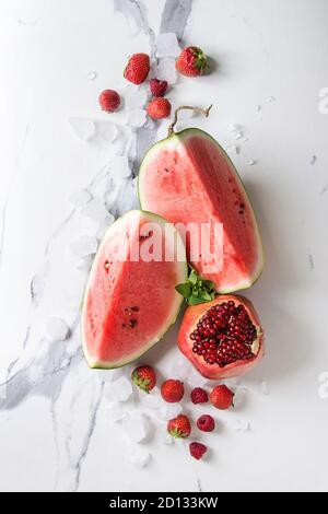 Varietà di rosso maturo frutta organica berry cocomero, fragola, lampone, melograno per cocktail o frullati con menta e ghiaccio frantumato su bianco Foto Stock