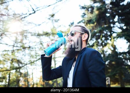 Uomo bearded che beve caffè nei boschi dopo il lavoro Foto Stock