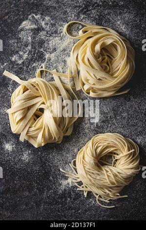 Varietà di artiginale raw pasta cruda spaghetti e tagliatelle con farina di semola su nero sfondo texture. Laici piana, spazio Foto Stock