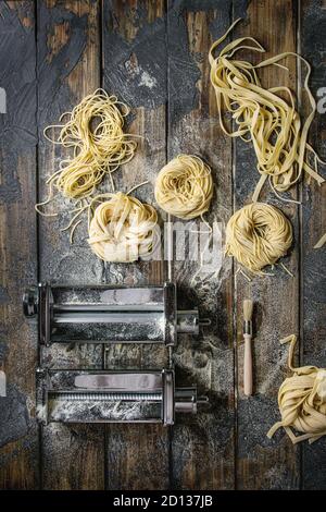 Varietà di artiginale raw pasta cruda spaghetti e tagliatelle con pasta maker macchina laminati e farina di semola su dark plank texture wo Foto Stock