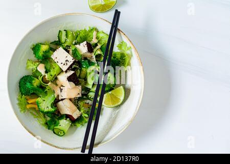 Insalata asiatica verde con broccoli, tofu affumicato e salsa di arachidi in una ciotola bianca, fondo bianco. Foto Stock