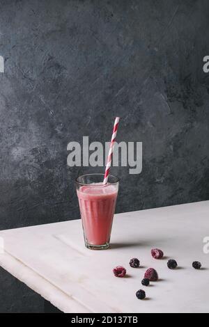 Un bicchiere di rosso di bacche Frutta anguria cocktail con paglia a strisce e frutti di bosco surgelati stand su marmo bianco tavola con muro grigio a sfondo. Su Foto Stock