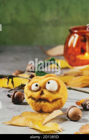 Funny craft ago Halloween zucca feltrato jack o lantern holiday decor con Giallo autunno foglie e ghiande su grigio Sfondo texture. Foto Stock
