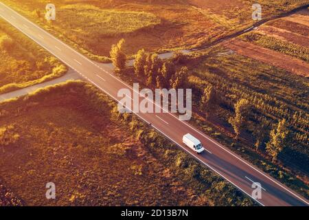 Vista aerea del minivan con consegna a domicilio sulla strada al tramonto estivo, drone pov del veicolo sulla strada attraverso la campagna Foto Stock