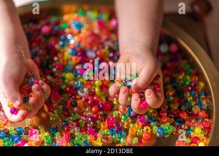 Perle colorate nei palmi del bambino. Uno sfondo molto colorato di perle scintillanti Foto Stock