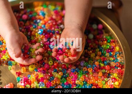 Perle colorate nei palmi del bambino. Uno sfondo molto colorato di perle scintillanti Foto Stock