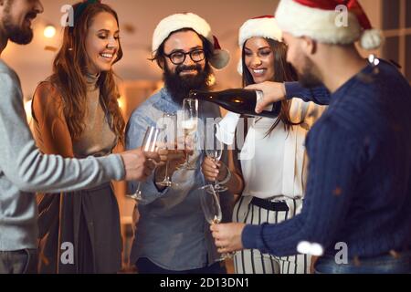 A Natale, un giovane uomo che versa champagne negli occhiali dei suoi amici O festa di Capodanno Foto Stock
