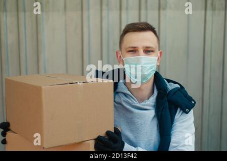 Felice uomo di consegna in una maschera protettiva guarda a. e contiene due scatole Foto Stock