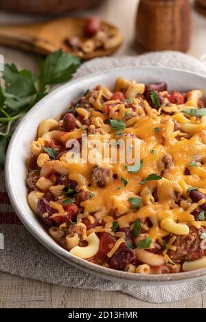 Primo piano di ciotola di maccheroni al peperoncino con formaggio cheddar fuso su un tavolo di legno Foto Stock