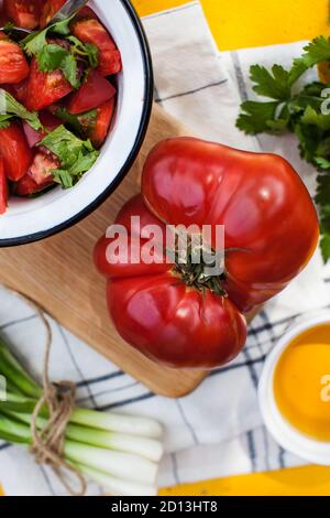 Pomodoro rosso carnoso gigante maturo su una tavola di legno, pomodoro e insalata verde in un piatto. Menu verdure, menu vegetariano. Foto Stock