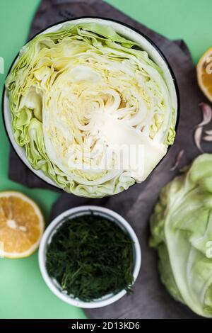 Cavolo bianco fresco e giovane in una sezione su sfondo verde, accanto a fette di aneto, aglio e limone. Foto Stock