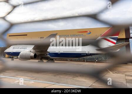 British Airways Boeing 747 Jumbo Jet aereo in classico schema centenario dietro recinzione. Messa a terra e ritirata a causa del COVID-19. Hangar di manutenzione Foto Stock