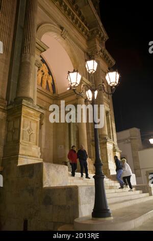 L'ingresso alla Basilica dei Santi Cosma e Damiano in Piazza Curri in tarda serata, Alberobello, Puglia, Italia, con persone che entrano e partono Foto Stock