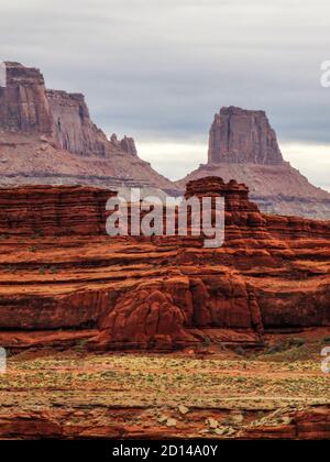 Erose scogliere brune rossastre scure, costituite dalla formazione di Moenkopi, lungo la strada del bordo bianco, Moab, Utah, USA, con un butte sullo sfondo Foto Stock