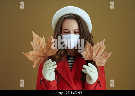 Ciao autunno. Donna elegante in camice rosso con foglia di acero giallo autunno isolato su sfondo beige. Foto Stock