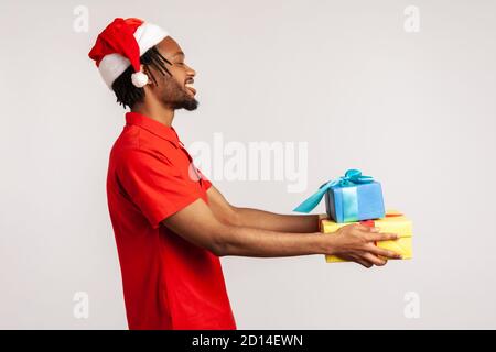 Profilo ritratto felice afro-americano ragazzo con dreadlock e nel cappello di babbo natale tenere le scatole presenti, la preparazione di regali su natale e nuovo voi Foto Stock