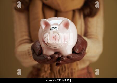 Ciao autunno. Closeup su donna in maglione con banca piggy su sfondo bronzeo. Foto Stock