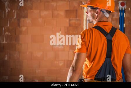 Caucasian Construction Industry Worker nei suoi anni '40 indossando Orange Hard Hat e occhiali di sicurezza in preparazione per un altro giorno intero sul cantiere. Foto Stock